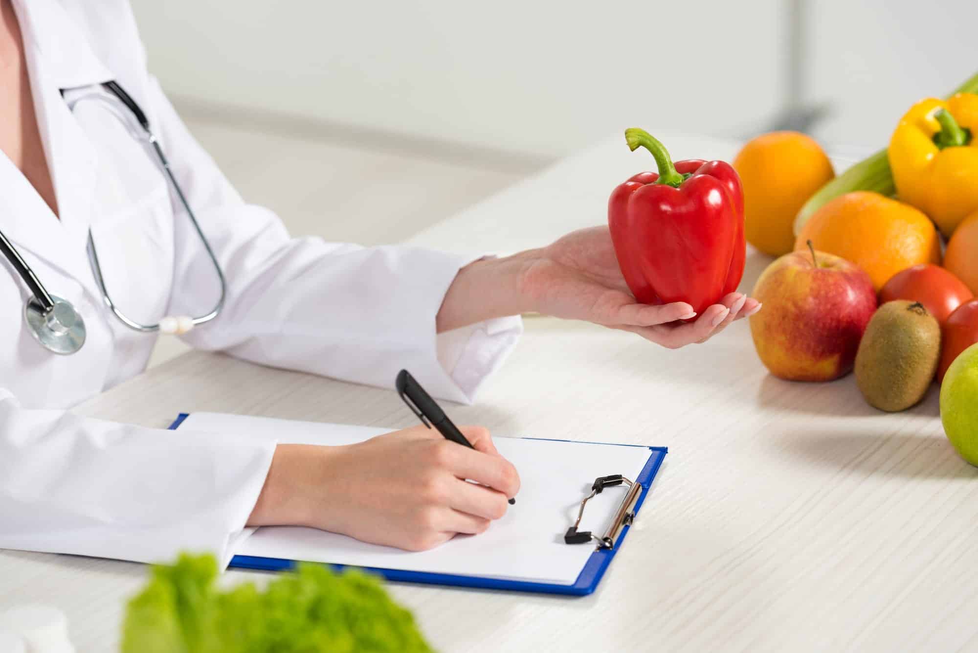 a doctor holding vegetables and writing on a sheet of paper that shows a wellness plan